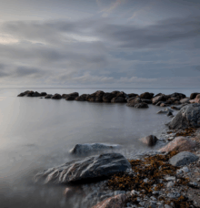 Kustlandskap med klippor och stilla vatten under en molnig himmel.