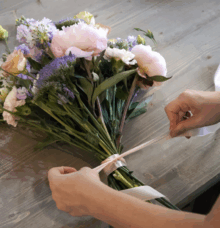 En person binder ett band runt en bukett med blommor på ett träbord.