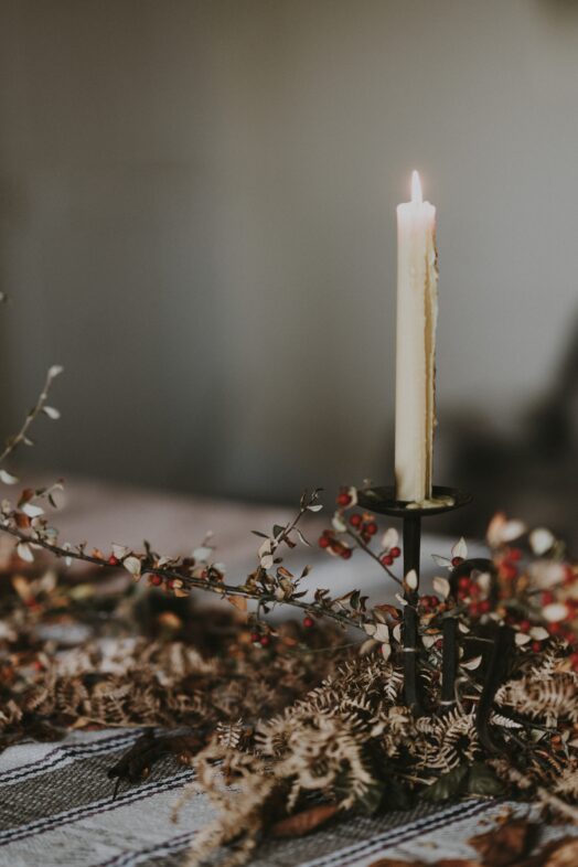 Ett ensamt, tänt ljus i en ljusstake omgiven av torkade blommor.